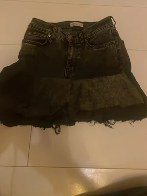 Svart volangkjol hemma sydd - Säljer en svart kortkjol från Proudly Jeans med volangdetalj nedtill. Kjolen har klassisk jeanslook med fickor fram och bak, samt rå kant längst ner för en edgy vibe. Perfekt för dig som gillar en tuff och trendig stil.