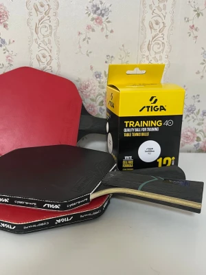Stiga pingisracket och bollar - Säljer två Stiga pingisracket, modell Cybershape, med svart och rött gummi samt ett 10-pack Stiga Training 40 pingisbollar. Racketarna har trähandtag med blå och turkosa detaljer. Perfekt för dig som vill träna eller spela pingis med vänner.