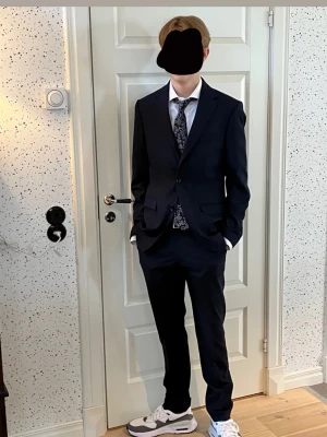 Mörkblå kostym med kavaj, skjorta och byxor - Snygg mörkblå kostym med klassisk kavaj och matchande byxor. Kavajen har två knappar. Skjortan (S) är från H&M, kavajen (46) och kostymbyxorna (44) är från Riley.  Nypris-2500 kr