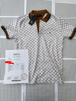 Rutig beige piké från Louis Vuitton - Snygg beige och vit rutig pikétröja från Louis Vuitton med bruna detaljer på krage och ärmslut. Klassisk pikéknäppning och diskret LV-logga på bröstet. Perfekt för dig som gillar exklusiv och trendig stil.