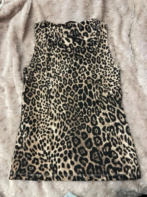 Leopardmönstrad ärmlös linnetopp - Snygg ärmlös linnetopp med leopardmönster i beige och svart. Toppen har en rak passform och är perfekt för dig som vill sticka ut med ett djurmönster. Materialet känns mjukt och stretchigt, vilket gör den bekväm att bära hela dagen.