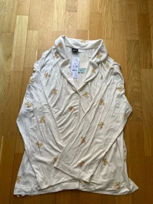 Ny pyjamasskorta  med nallemönster Gina Tricot - Supersöt ny  pyjamaströja från Gina Tricot med gulligt nallemönster över hela plagget. Mjuk och skön kvalitet med 'soft touch'-känsla, knäppning framtill och klassisk krage. Perfekt för mysiga hemmakvällar. Storlek xl men passar m-xl. 