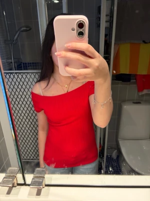 Röd ribbad offshoulder topp - Trendig röd ribbad topp med offshoulder-design. Toppen är figurnära och har korta ärmar, perfekt för att skapa en snygg och ungdomlig look. Materialet är stretchigt och bekvämt, vilket gör den enkel att bära till jeans eller kjol.