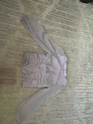 Ljuslila stickad tröja med volang - Supersöt ljuslila stickad tröja med volangdetaljer längs sidorna och vid nederkanten. Tröjan har rund halsringning och långa ärmar. Perfekt för dig som gillar en feminin och trendig stil.