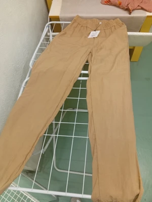 Beige linnebyxor från Saint Tropez - Snygga och avslappnade beige linnebyxor från Saint Tropez med elastisk midja och raka ben. Perfekta för en chill och stilren look. Materialet är linne som ger en luftig känsla och byxorna har en enkel design utan fickor eller detaljer.