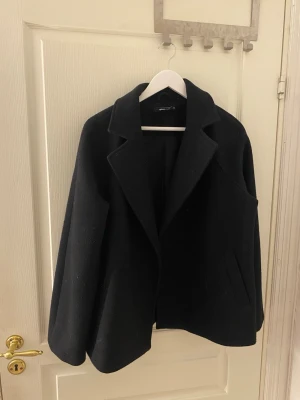 Svart ullkappa från Weekday - Säljer en Stilren svart kappa från Gina tricot i ullblandning med klassisk krage och raka snitt. Kappan har diskreta sidofickor och en enkel, minimalistisk design som passar perfekt till höstens och vinterns outfits. Storlek XS men passar även S