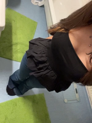 Svart axelbandslös topp - Snygg svart axelbandslös topp med volangdetalj i midjan. Toppen har en bandeauformad överdel och är perfekt för att skapa en trendig look. Passar till både jeans och kjol för en cool outfit.