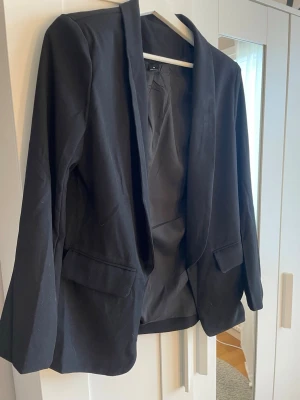 Svart kavaj med klassisk passform - Stilren svart kavaj med lång ärm och klassisk krage. Kavajen har två fickor framtill och är helfodrad.