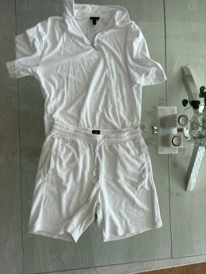 Vit set från HM - Ett set från HM som jag nu säljer. Kläderna är av Handduks Material. Shortsen är i storlek L och Överdelen i storlek M.  Överdelen är knappt använd, ca 1-2ggr. Shortsen är mer använda men är fortfarande i bra skick.  Passar perfekt för en skön sommardag  Nypris var ca 600 för hela.