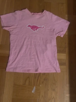 Rosa t-shirt  - Säljer en rosa t-shirt med ett coolt tryck i mitten av bröstet. T-shirten har korta ärmar och en klassisk passform. Perfekt för dig som gillar unika motiv och vill sticka ut lite extra. Tröjan är i storlek 140-150 men kan även gå om man har Xxs, ror på hur man vill att den ska sitta på. 