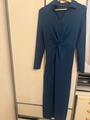 Blå långklänning från SHEIN - Långärmad blå långklänning från SHEIN med krage och knappar framtill. Klänningen har twistad detalj i midjan och är tillverkad i ett strukturerat, stretchigt material. Perfekt för dig som gillar enkel men snygg stil.