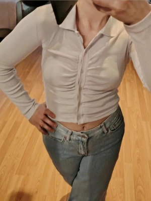 Vit topp/blus med knappar🤍😍  - Trendig vit långärmad blus med långa ärmar och krage. Toppen har knappar framtill och snygg rynkning längs mitten som ger en cool effekt🤩. Perfekt till jeans eller kjol för en modern look💎 