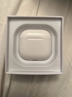 Vita trådlösa hörlurar Apple AirPods 4 - Säljer ett par vita trådlösa hörlurar från Apple, modell AirPods 4 , med laddningsetui i blank plast. Snygg och kompakt design som är enkel att ta med sig. Perfekt för musik, poddar och samtal på språng.