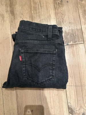 Levi's 502 svarta regular taper jeans - Säljer ett par svarta Levi's 502 Regular Taper jeans med klassisk femficksdesign och röd Levi's-tag på bakfickan. Jeansen har normal passform med avsmalnande ben och är tillverkade i slitstark denim. Perfekta för en avslappnad och stilren look.