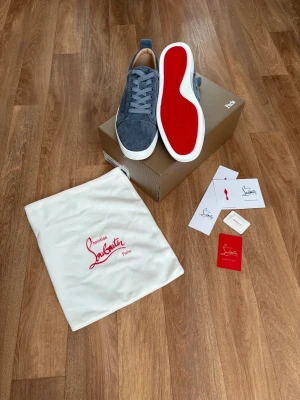 Blåa Christian Louboutin sneakers - Snygga gråa sneakers från Christian Louboutin med klassisk röd sula och vita kanter. Ovandelen är i mocka och skorna har gråa skosnören. Kommer med originalpåse och tillbehör. Perfekta för dig som vill sticka ut med exklusiva detaljer.Hör av dig vid minsta lilla