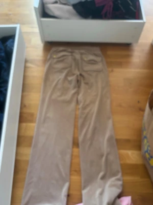 Beige velourbyxor Juicy Couture XXS - Säljer ett par beige mjukisbyxor från Juicy Couture i velour. Byxorna har utsvängda ben och resår i midjan. Perfekta för en chill och trendig look. Klassisk Juicy Couture-stil med mjukt material och snygg passform.