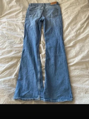 Blå bootcut jeans med retro vibe - Lågmidjade Bootcut jeans från junkyard. Säljer ett par blå bootcut jeans med klassisk femficksdesign och utsvängda ben. Jeansen har en ljusblå tvätt och är tillverkade i denim. Perfekt för dig som gillar en cool och avslappnad stil.