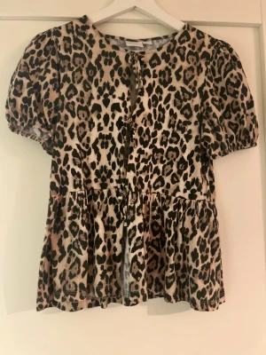 Leopardmönstrad tröja - Trendig blus/tröja med leopardmönster i beige och svart. Modellen har korta puffärmar, rund halsringning och knytning framtill. Blusen har en lös passform och volang nedtill. 