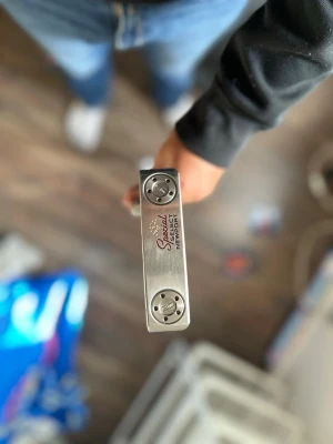 Scotty Cameron Special Select Newport - Säljer en silverfärgad putter från Scotty Cameron, modell Special Select Newport. Klubban har detaljer i rött och svart samt inskriptioner på klubbhuvudet. Tillverkad i metall och har en klassisk, stilren design för golfspel. Orginal grepp ingår, upphämtning sker i Södertälje. Hör av er vid frågor☺️