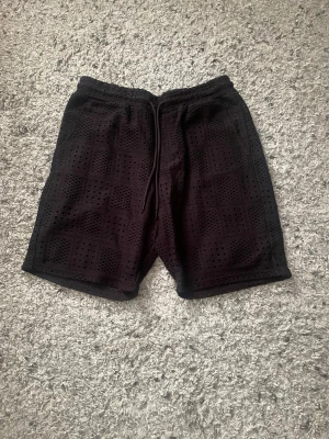 Svarta shorts  - Svarta shorts med coolt perforerat mönster och snörning i midjan. Perfekta för sommaren och har en avslappnad passform. Materialet känns lätt och luftigt, vilket gör dem sköna att bära varma dagar.