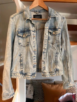 Ljusblå jeansjacka från Stradivarius - Säljer en ljusblå jeansjacka från Stradivarius i klassisk modell med två bröstfickor med knappar och snygga sömdetaljer. Jackan har krage och metallknappar framtill. 