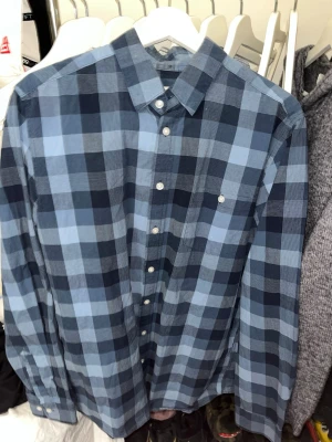 Blå rutig skjorta från Dressmann - Snygg blå rutig skjorta från Dressmann med klassisk krage och vita knappar. Skjortan har lång ärm och är tillverkad i mjuk bomull, perfekt för en avslappnad men stilren look.