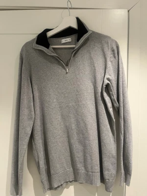 Grå zip-tröja från MNG - Snygg grå långärmad tröja från MNG med halvzip och ribbade muddar. Tröjan har en svart detalj på insidan av kragen och är tillverkad i mjukt material som passar perfekt för lager-på-lager. Enkel och stilren design.priset kan diskuteras och storleken passar m 