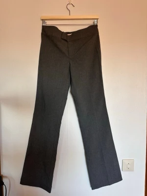 Grå kostymbyxor med bootcut - Snygga grå kostymbyxor med  låg midja. Byxorna har en klassisk design utan synliga fickor och är tillverkade i ett tunt material. Perfekta för dig som vill ha en stilren och tidlös byxa.
