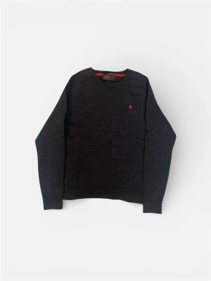 Mörkgrå stickad tröja Morris - Snygg mörkgrå stickad tröja från Morris med rund halsringning och röd broderad logga på bröstet. Tröjan har långa ärmar och ribbade muddar vid ärmslut och nederkant. Perfekt till höst och vinter för en stilren look.