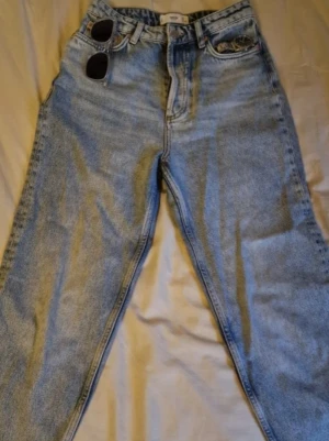 Ljusblå raka jeans med hög midja - Säljer ett par ljusblå jeans med rak passform och hög midja. Klassisk femficksmodell och dragkedja fram. Jeansen har en avslappnad vintage-look och är perfekta för en trendig vardagsstil. Materialet är denim i bomull.