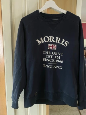 Marinblå sweatshirt från Morris - Snygg marinblå sweatshirt från Morris med broderad text och brittisk flagga på bröstet. Tröjan har rund halsringning, ribbade muddar och klassisk passform. Perfekt för en stilren och avslappnad look. Herr storlek. Stl S #vinted #vintedsverige #märkeskläder #brandclothes #designer #menswear #herrkläder #original #äkta #secondhand #preloved #hållbartmode #streetwear #fashionformen #outfitformen #klädertillsalu #säljes #fynd #braSkick #snabbaffä
