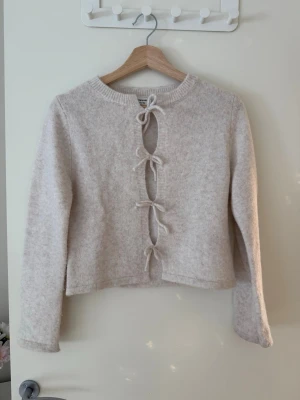 Beige stickad tröja med rosetter framtill. - Supersöt beige stickad tröja med fyra rosetter framtill