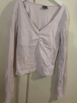 Ljusrosa v-ringad topp med rynk - Trendig ljusrosa topp med v-ringning och snygg rynkdetalj framtill. Långärmad modell i mjukt bomullsmaterial, perfekt för att styla med jeans eller kjol. Enkel men ändå chic design som passar till många olika looks.