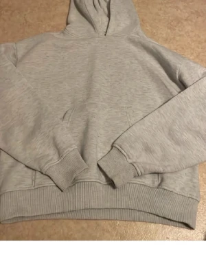 Ljusgrå basic hoodie - En enkel och stilren ljusgrå hoodie med huva och magficka. Hoodien har ribbade muddar vid ärmslut och nederkant, samt en relaxed passform som passar perfekt till vardagslooken.