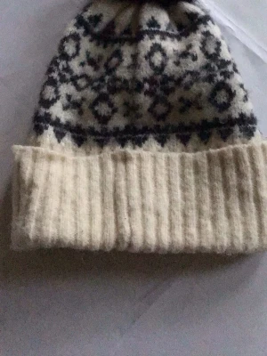 Vit och blå mönstrad stickad mössa - Säljer en mysig stickad mössa i vitt med blått mönster och bred vikt kant. Mössan har klassiskt nordiskt mönster och är gjord i mjukt, tjockt material som håller värmen. Perfekt för kalla dagar och ger en snygg vinterlook.