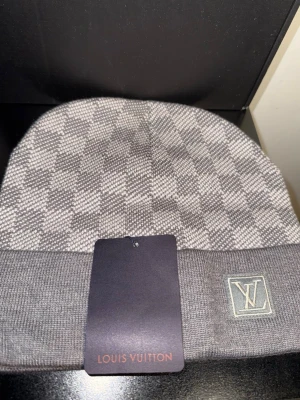 Grå Lv mössa  - Snygg grå mössa från LV med klassiskt rutmönster och vikt kant. LV-logga broderad framtill. Tillverkad i mjukt stickat material som håller dig varm och stilren under kalla dagar.