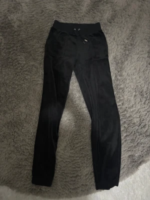 Svarta mjukisbyxor med snörning - Svarta mjukisbyxor i mjukt material med bred resår och snörning i midjan. Framtill finns två stora fickor och baktill två fickor med knappstängning. Byxorna har en slim passform och är perfekta för chill dagar.