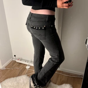 Svarta jeans med pärldetaljer - Säljer ett par svarta jeans med raka ben och snygga pärldetaljer på bakfickorna och vid bensluten. Jeansen har klassisk femficksdesign och stängs med knapp och dragkedja. Perfekta för dig som vill sticka ut lite extra! Storlek 28, sytt t bootcut
