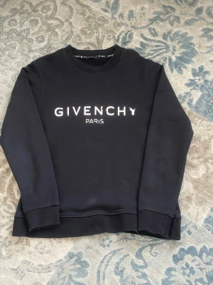 Svart sweatshirt från Givenchy Paris - [FRI FRAKT 🚚]Svart sweatshirt från Givenchy Paris med vit logotyp framtill. Tröjan har rund halsringning, långa ärmar och ribbade muddar vid ärmslut och nederkant. Perfekt för en stilren och trendig look. Står L men ej helt säker på det 