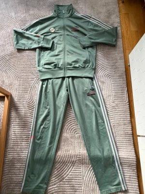 Adidas x Star Wars Boba Fett tracksuit - En fet Adidas Firebird tracksuit som för mig varit brutal komplimangmagnet 🔥 Storlek m på top och byxor. Gjord i samarbete mellan Adidas och Lucasfilm, baserad på Boba Fett från Star Wars. Topen är i bra skick med ett litet hål på ena armen. Byxorna är i dugligt skick, dragkedjorna på byxorna är skickligt bytta men skrevet behöver repareras. Även byxsluten har två revor. För den som älskar att modifiera kläder kan denna tracksuit bäras i många år till och fortsätta generera komplimanger.