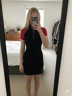 Svart och röd kortklänning med dragkedja - Sportig kortklänning från H&M i svart med röda ärmar och vita detaljer. Klänningen har en tight passform, korta ärmar och en snygg dragkedja framtill med ringdetalj. Perfekt för en trendig och avslappnad look.