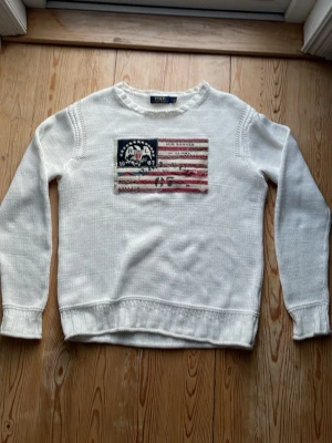 stickad tröja Polo Ralph Lauren - Vit stickad tröja från Polo Ralph Lauren med amerikansk flagga. Den funkar även för M.