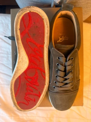 Grå mockasneakers från Louboutin - Snygga grå/gröna sneakers från Christian Louboutin i mjuk mocka med klassisk röd sula och breda grå skosnören. Storlek 41,5. 