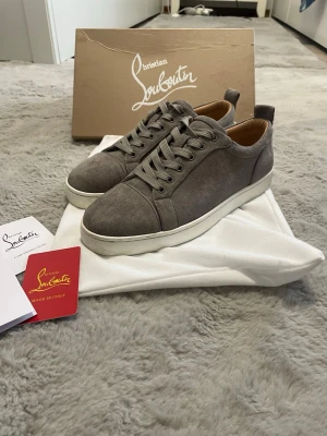 Christian Louboutin Sneakers Grå - Christian Louboutin sneakers i grå mocka med signatur-röda sulor. Levereras med originalkartong och dust bag.  ⭐️ Skick: 8/10 (Lätt slitage på sulorna) 🎲 Storlek: 42 🎨 Färg: Grå 📦 Snabb och noggrann frakt.