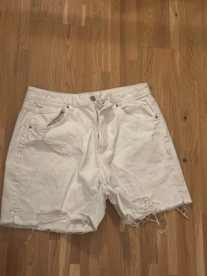 Vita denimshorts från Sinsay - Vita denimshorts från Sinsay med råa, fransiga benslut och slitna detaljer framtill. Klassisk femficksmodell med knapp och dragkedja. Perfekta för en avslappnad och trendig sommarlook.