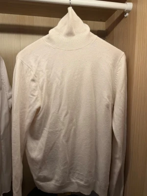 Massimo dutti polotröja  - Klassisk vit stickad polotröja med lång ärm och ribbad hög krage. Tröjan har en enkel och stilren design, perfekt för lager på lager. Materialet ser mjukt och bekvämt ut, och passformen är rak med ribbade muddar vid ärmslut och nederkant. ✨