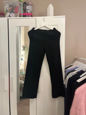 Svarta vida kostymbyxor - Säljer ett par svarta kostymbyxor med hög midja och vida ben. Byxorna har pressveck framtill för en clean look och är sydda i ett slätt, mjukt tyg som ger en dressad känsla. Perfekta till en snygg topp eller skjorta.