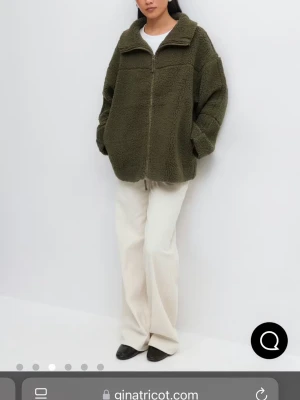 Olivgrön teddyjacka från Gina Tricot - Mysig olivgrön teddyjacka från Gina Tricot med dragkedja framtill och hög krage. Jackan har en oversized passform, nedhasade axlar och är gjord i fluffigt teddy-material som ger en cool och avslappnad look.