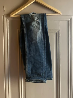 Dondup jeans  - Säljer ett par blå slim fit dondup jeans med slitningar och tvättade detaljer. Jeansen har klassisk femficksdesign och raka ben. Materialet är denim i bomull. Perfekta för en avslappnad och trendig look.