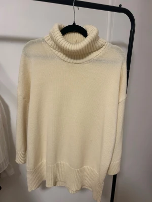 Krämvit polotröja i oversize - Säljer en krämvit stickad polotröja i oversize-modell. Tröjan har bred ribbad polokrage, ribbade muddar och avslappnad passform med sänkta axlar. Perfekt för lager på lager och riktigt mysig.